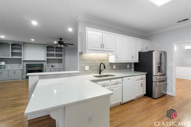 kitchen with white dishwasher, a peninsula, a sink, visible vents, and stainless steel fridge