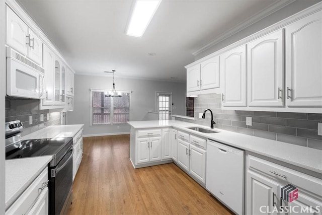 kitchen with a peninsula, white appliances, white cabinets, and a sink