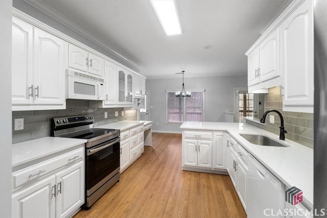 kitchen featuring a peninsula, white appliances, white cabinetry, and a sink