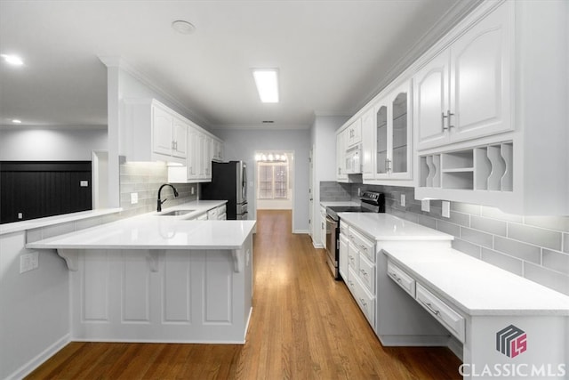 kitchen with a breakfast bar area, appliances with stainless steel finishes, white cabinetry, a sink, and a peninsula