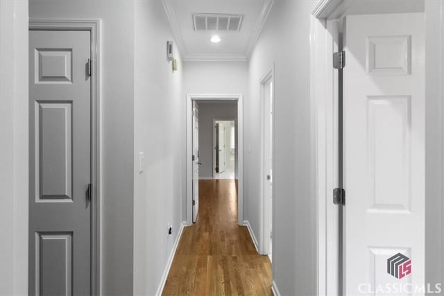 corridor featuring ornamental molding, visible vents, baseboards, and wood finished floors