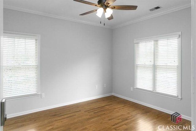 empty room with a wealth of natural light, ornamental molding, wood finished floors, and visible vents