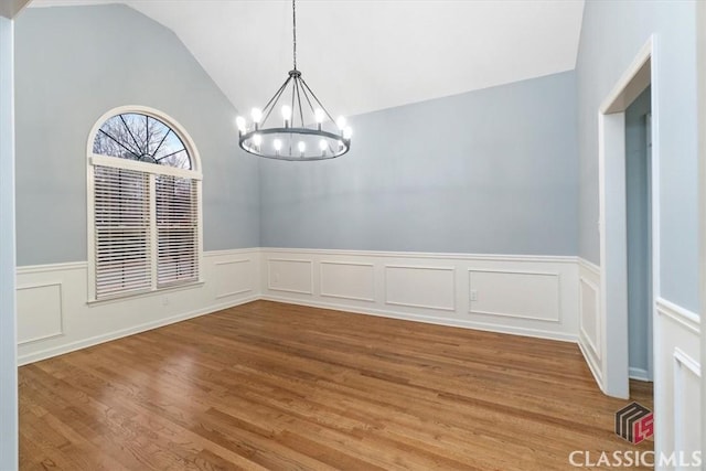 unfurnished room with an inviting chandelier, vaulted ceiling, wood finished floors, and a wainscoted wall