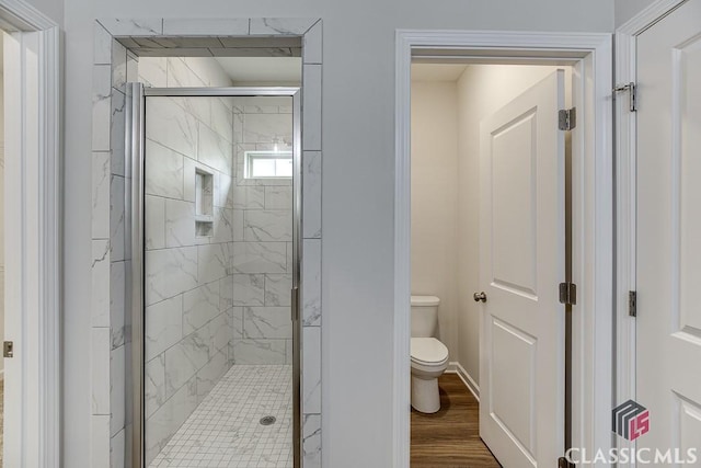 bathroom with wood finished floors, a marble finish shower, and toilet