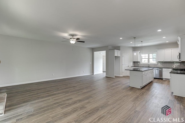 kitchen featuring open floor plan, appliances with stainless steel finishes, a center island, dark countertops, and dark wood finished floors