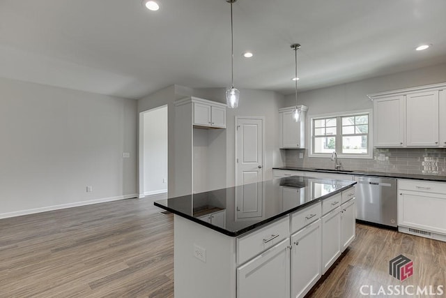 kitchen with tasteful backsplash, dark countertops, wood finished floors, stainless steel dishwasher, and a sink