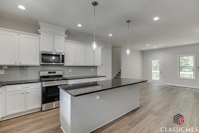 kitchen with dark countertops, backsplash, appliances with stainless steel finishes, a kitchen island, and light wood-type flooring