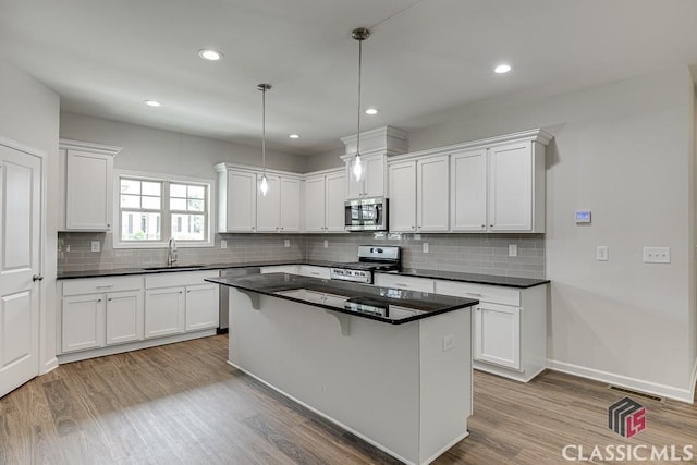 kitchen with appliances with stainless steel finishes, dark countertops, a sink, and light wood-style floors