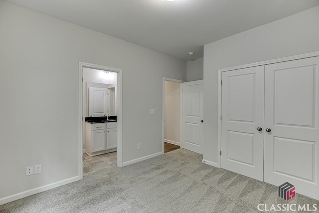 unfurnished bedroom featuring a closet, light carpet, baseboards, and ensuite bathroom