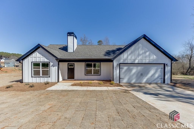 modern farmhouse with an attached garage, concrete driveway, roof with shingles, board and batten siding, and a chimney