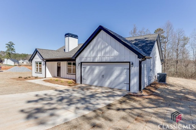 modern farmhouse style home featuring a garage, concrete driveway, a chimney, cooling unit, and board and batten siding