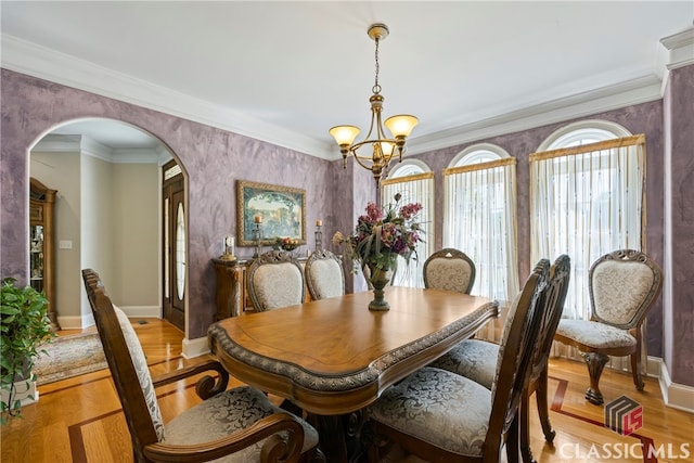 dining space with arched walkways, baseboards, light wood-style floors, ornamental molding, and an inviting chandelier