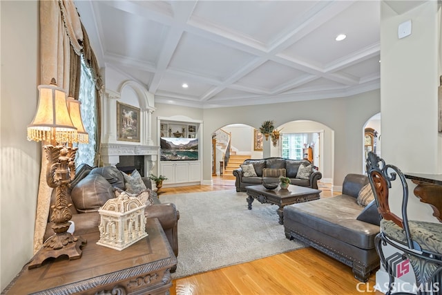 living room with arched walkways, light wood-style flooring, coffered ceiling, stairway, and beam ceiling