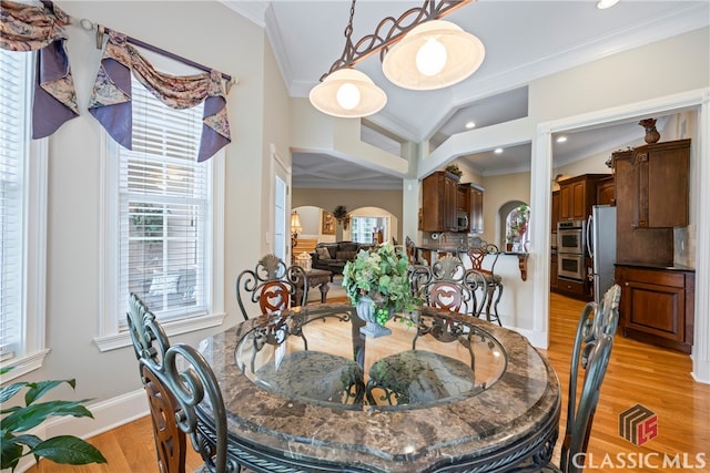 dining space featuring a healthy amount of sunlight, light wood-style flooring, arched walkways, and crown molding