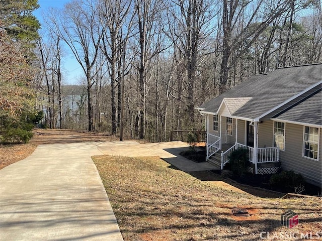 view of yard featuring a view of trees, a porch, and driveway