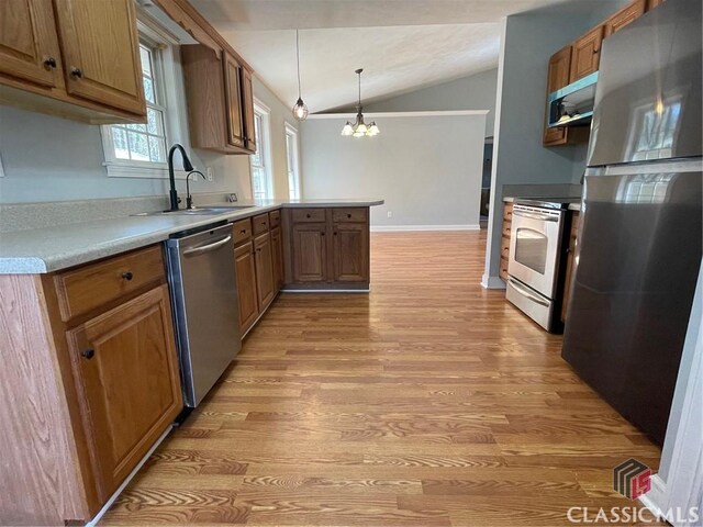 kitchen with light wood finished floors, vaulted ceiling, a peninsula, stainless steel appliances, and a sink