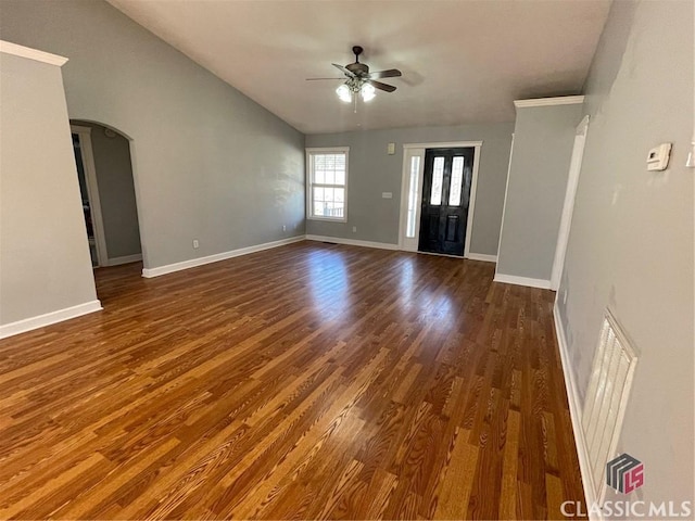 unfurnished living room with dark wood-type flooring, baseboards, vaulted ceiling, arched walkways, and a ceiling fan