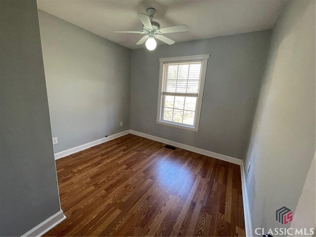 empty room featuring dark wood finished floors, visible vents, and baseboards