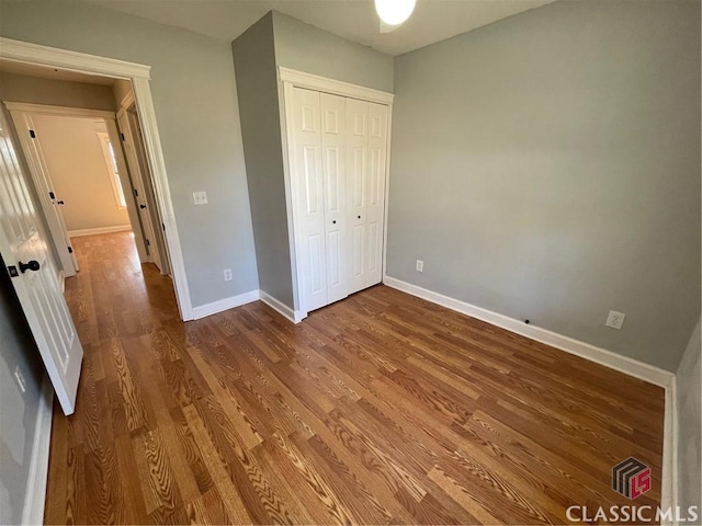 unfurnished bedroom with wood finished floors, baseboards, and a closet