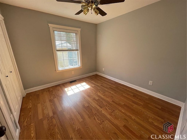 spare room with a ceiling fan, visible vents, dark wood-style floors, and baseboards