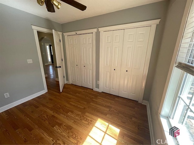 unfurnished bedroom with baseboards, multiple closets, wood finished floors, arched walkways, and a ceiling fan