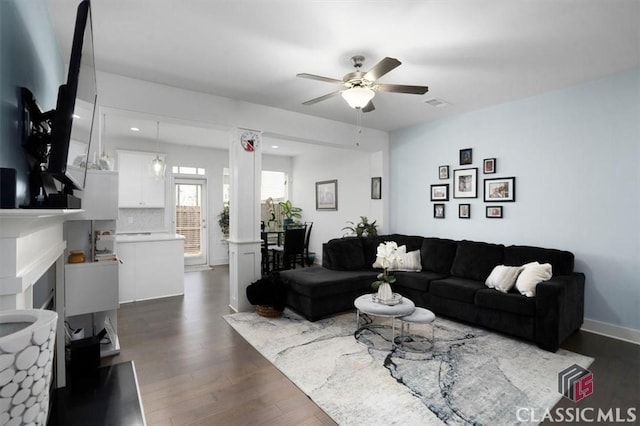 living room with visible vents, a ceiling fan, a fireplace, and dark wood-style flooring