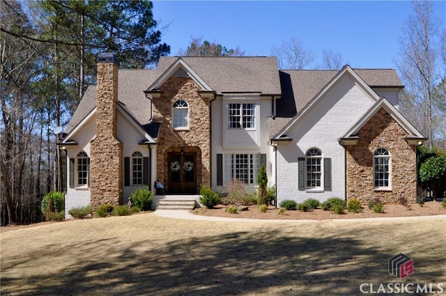 view of front of property featuring french doors, brick siding, roof with shingles, and a chimney