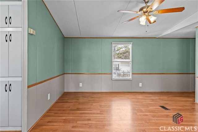 spare room featuring visible vents, a decorative wall, a ceiling fan, and wood finished floors