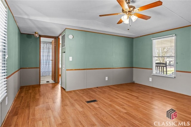 empty room with vaulted ceiling, visible vents, a ceiling fan, and wood finished floors