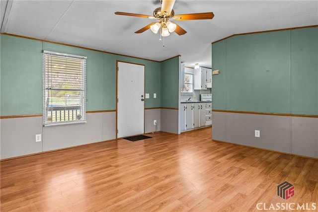 empty room with light wood finished floors, ornamental molding, ceiling fan, and vaulted ceiling