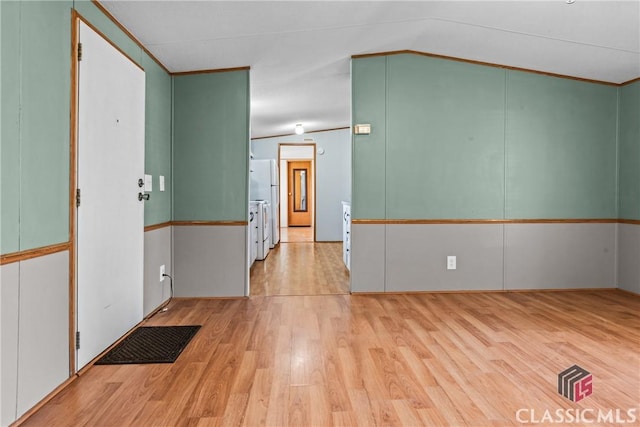 empty room with light wood-type flooring, lofted ceiling, and ornamental molding