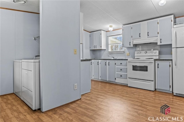 kitchen featuring light wood-type flooring, under cabinet range hood, dark countertops, white appliances, and washing machine and clothes dryer