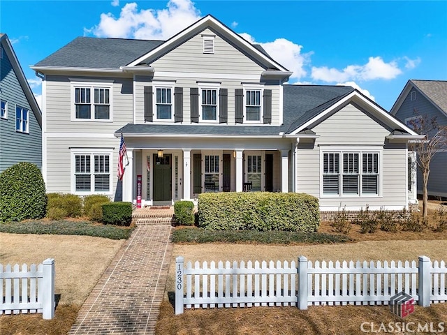 traditional-style house featuring a porch, a shingled roof, and fence