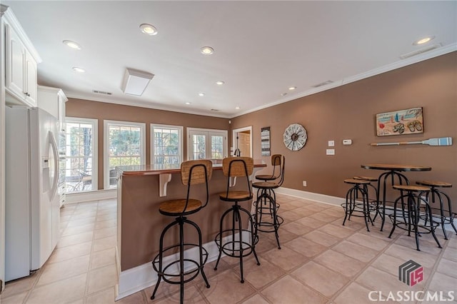 kitchen featuring white cabinets, a breakfast bar area, recessed lighting, white refrigerator with ice dispenser, and ornamental molding