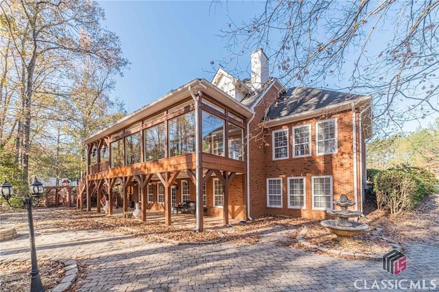 back of property featuring a chimney, a sunroom, a patio, and brick siding