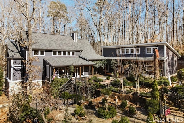 back of property with stairs, a chimney, and a shingled roof