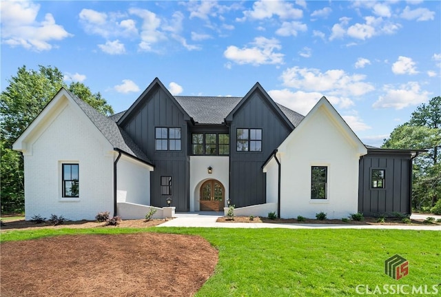 modern farmhouse with brick siding, board and batten siding, a front yard, and roof with shingles