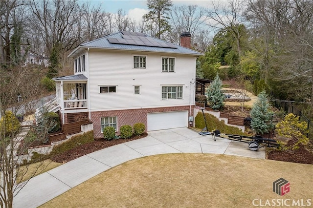 view of front facade with a front lawn, roof mounted solar panels, metal roof, brick siding, and a chimney