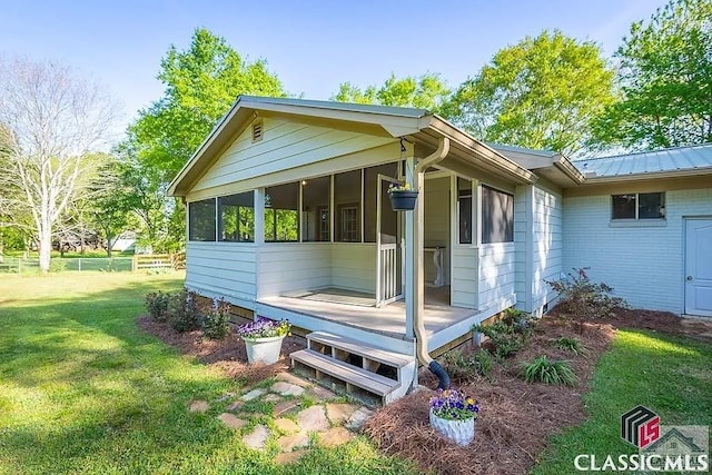 view of side of home featuring fence, a yard, a sunroom, brick siding, and metal roof