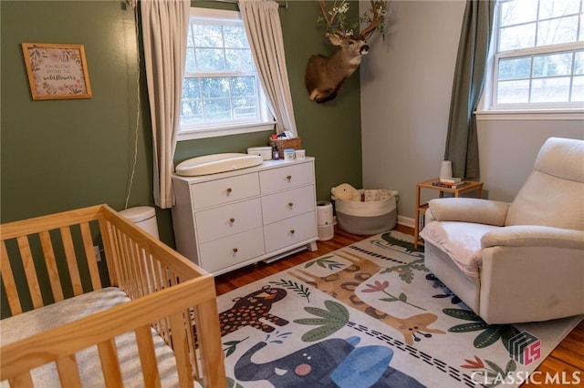 bedroom featuring a nursery area, dark wood-style floors, and baseboards