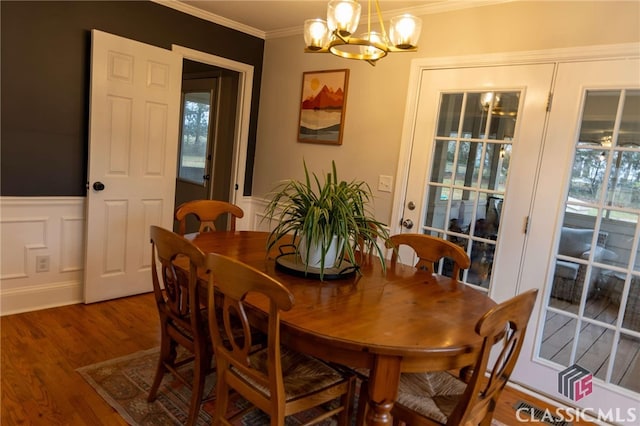 dining area featuring wood finished floors, a wainscoted wall, ornamental molding, a decorative wall, and a chandelier