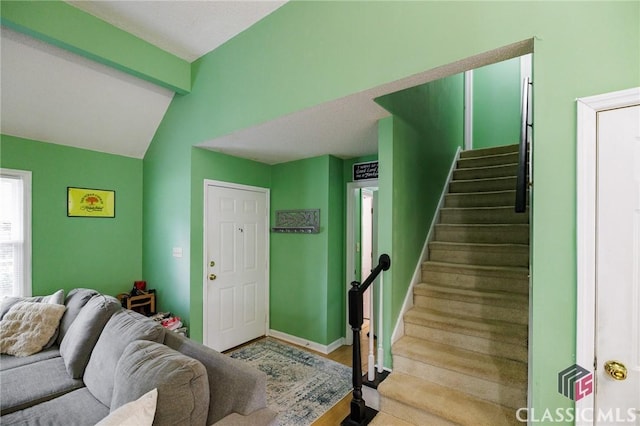 living area with stairs, baseboards, and vaulted ceiling with beams