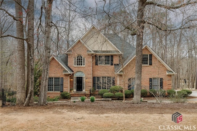 view of front of property featuring brick siding, a shingled roof, and fence