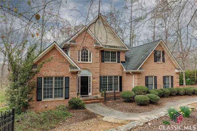 view of front of property with fence, brick siding, and roof with shingles