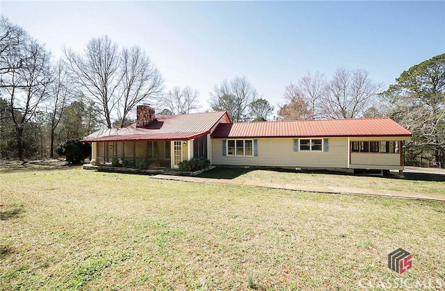 view of front of house featuring a chimney, a sunroom, a front lawn, and metal roof