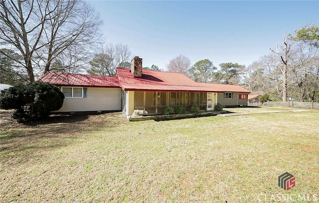 back of house with metal roof, a lawn, a chimney, and fence