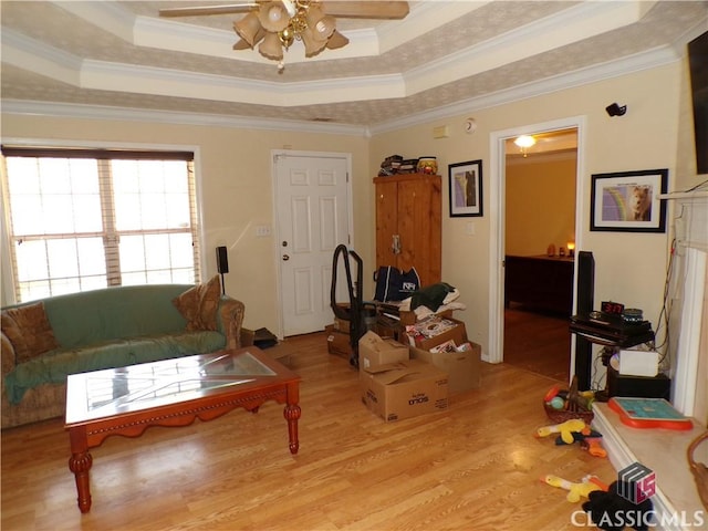 living area with light wood-style flooring, ceiling fan, a tray ceiling, and ornamental molding