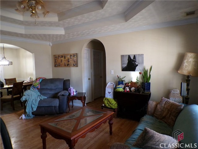 living area with a tray ceiling, wood finished floors, and arched walkways