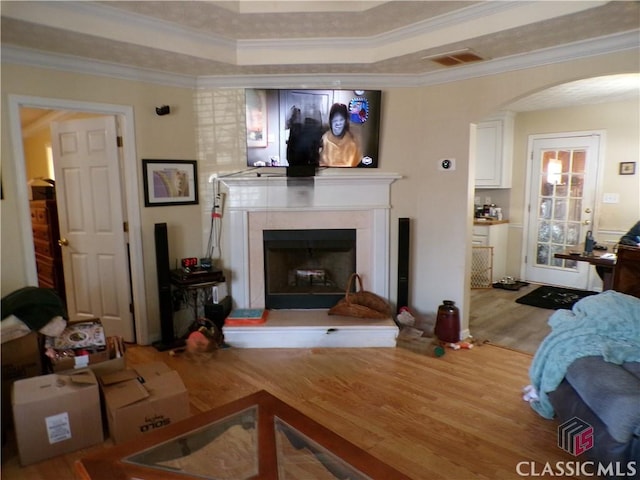 living area with crown molding, wood finished floors, arched walkways, and a tray ceiling