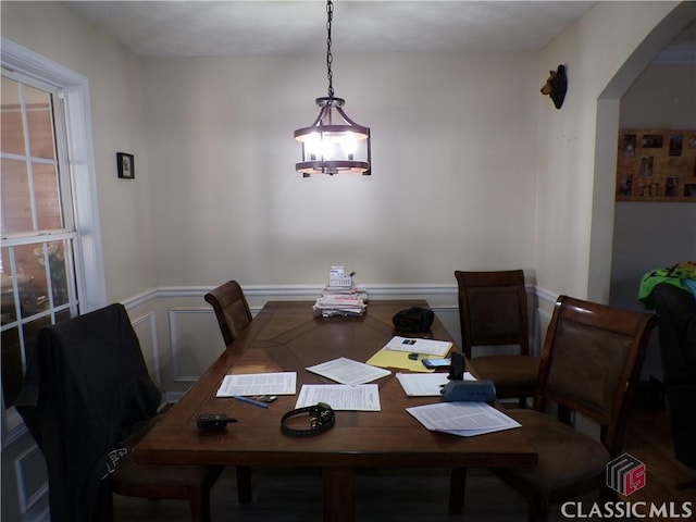 dining area featuring a decorative wall, wainscoting, arched walkways, and a chandelier